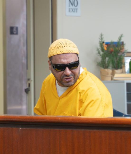 Man in yellow jail jumpsuit with sunglasses on speaking over his left shoulder