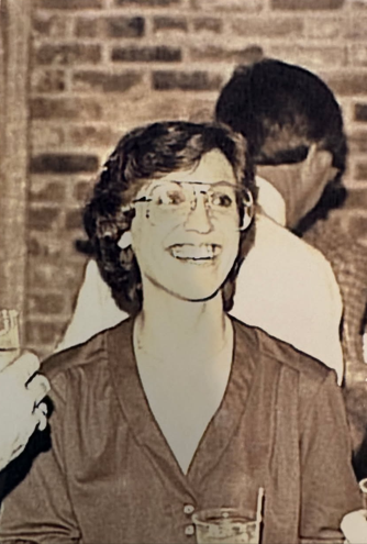 Woman smiling looking off to her left with 70s/80s style glasses on. The photo is sepia toned.