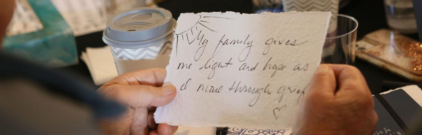 Woman holding handwritten paper saying "My family gives me light and hope as I move through grief."