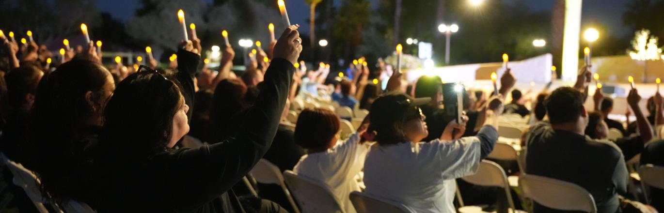 Crowd sitting facing a stage holding candles in the air