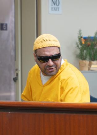 Man in yellow jail jumpsuit with sunglasses on speaking over his left shoulder